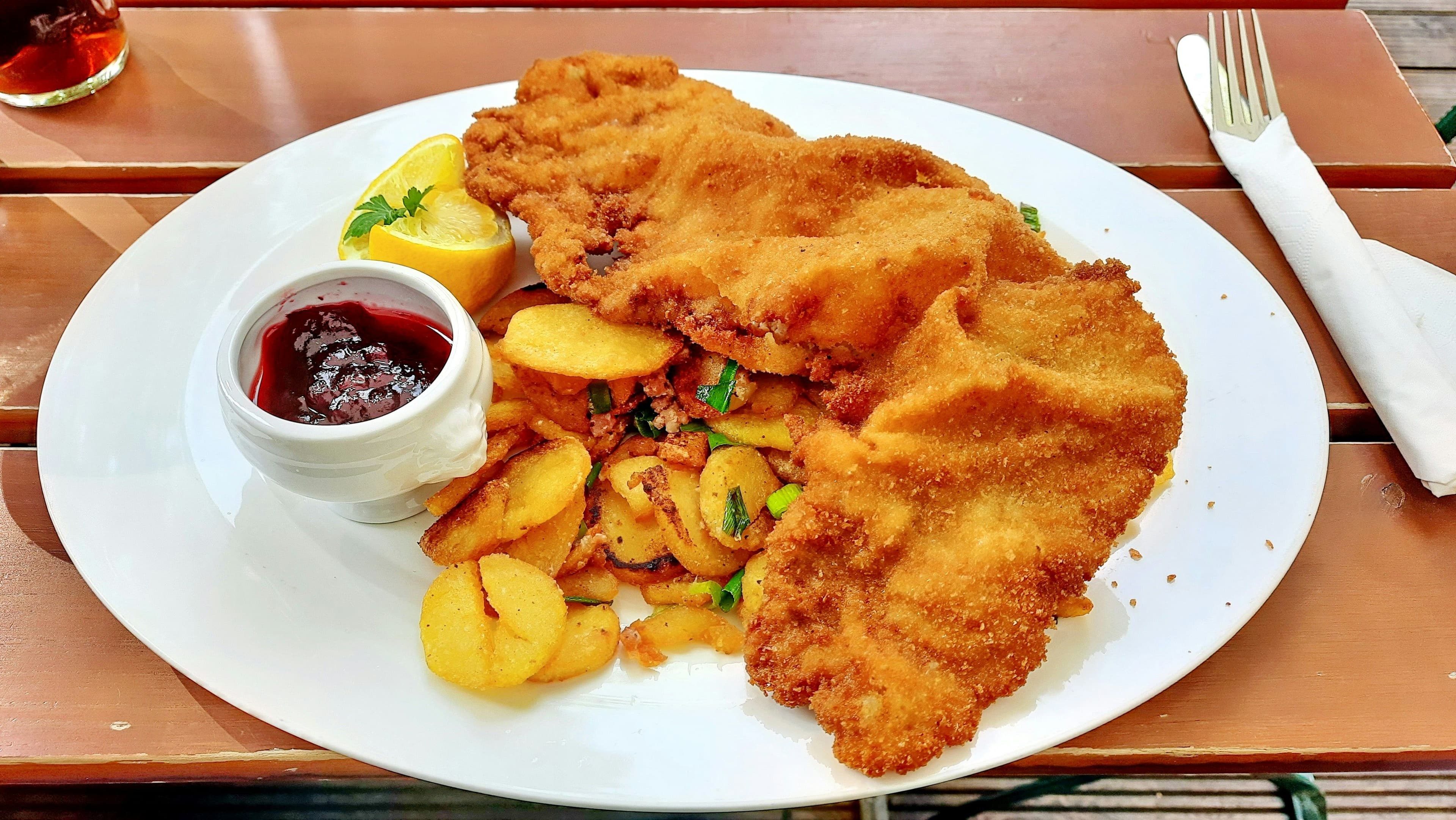 Ein Schnitzel, Bratkartoffeln und eine Schale mit Preiselbeeren auf einem Teller