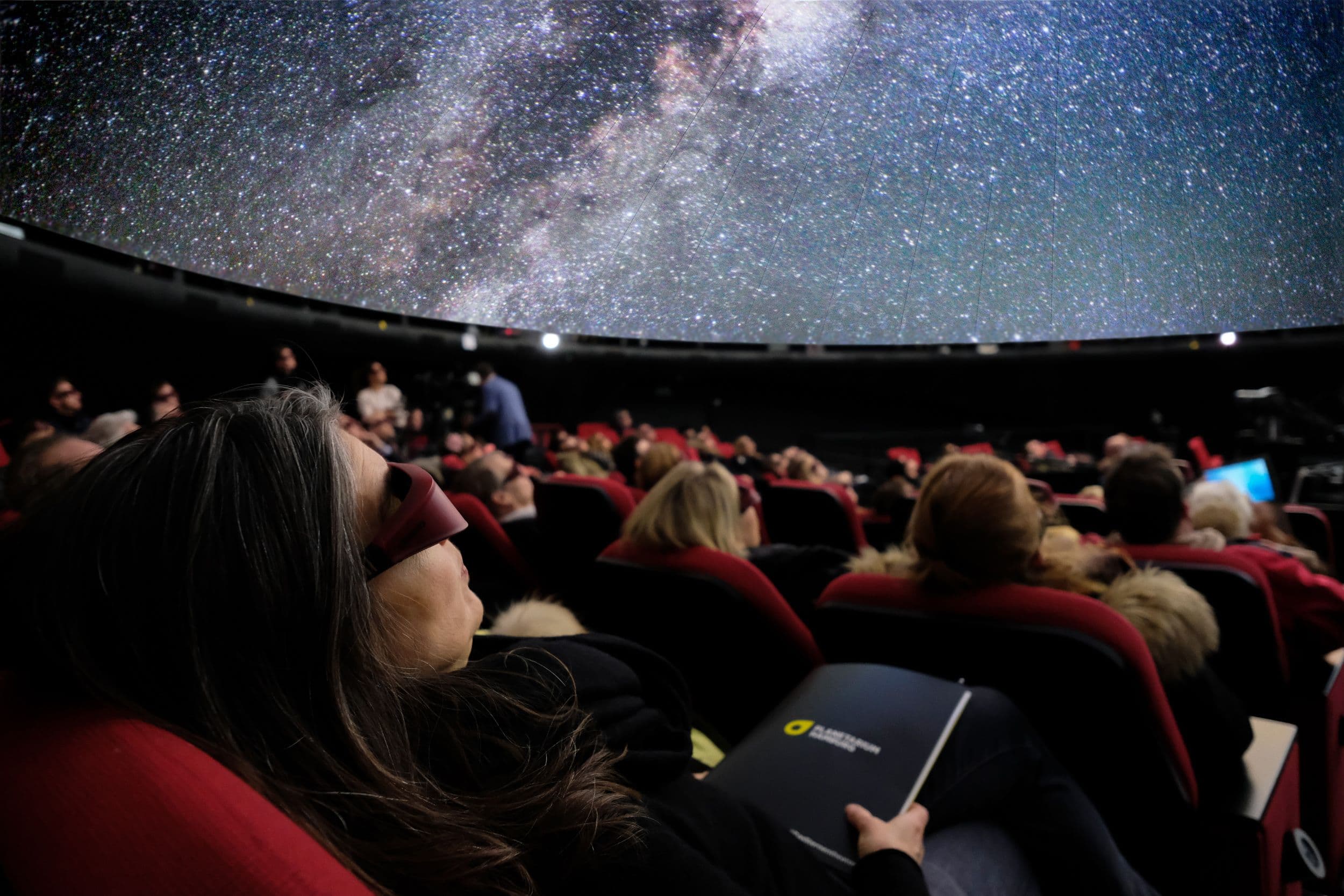 Menschen sitzen im Planetarium und schauen in die Sternenkuppel