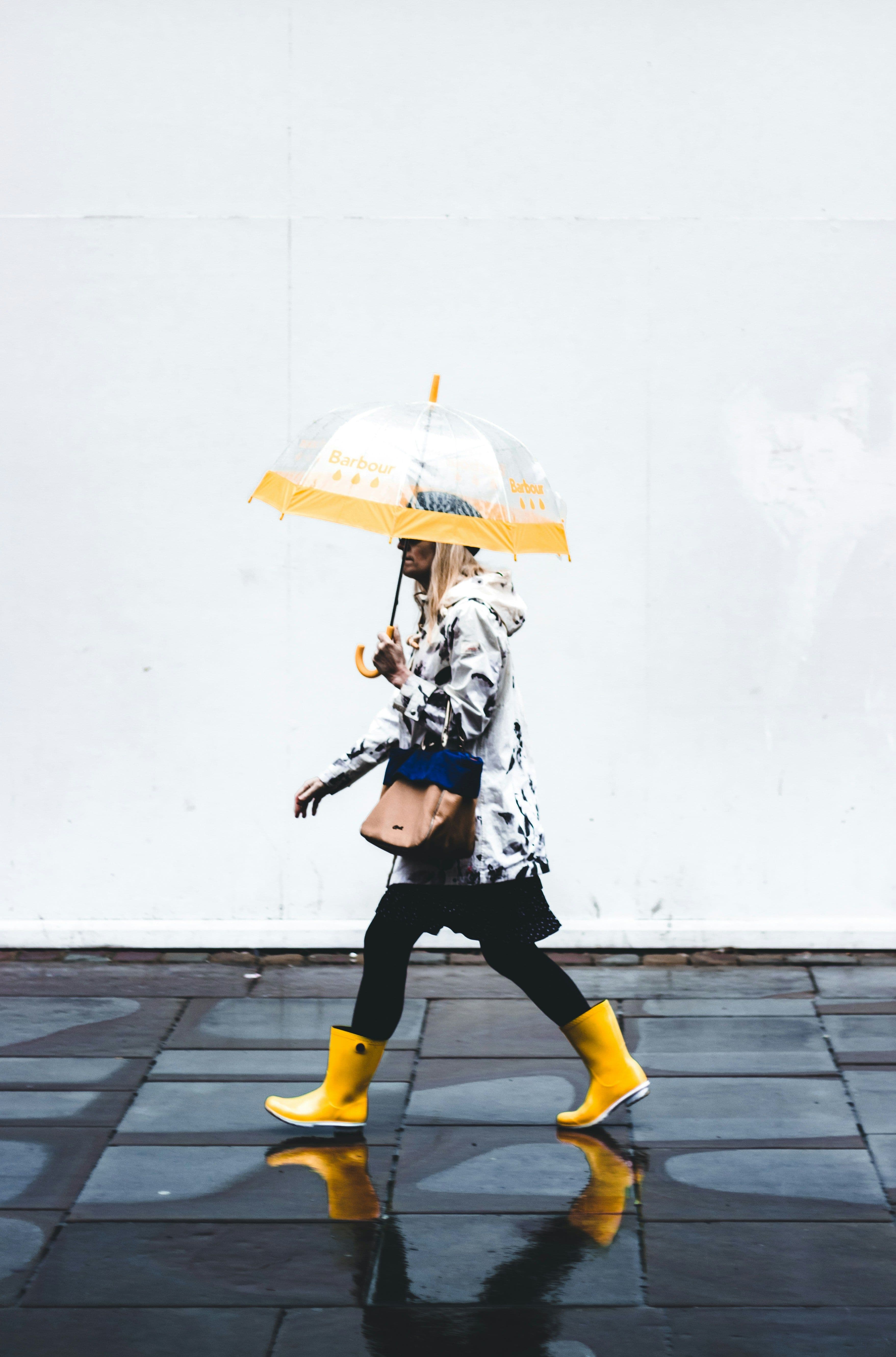 Frau spaziert mit Regenschirm und Gummistiefeln