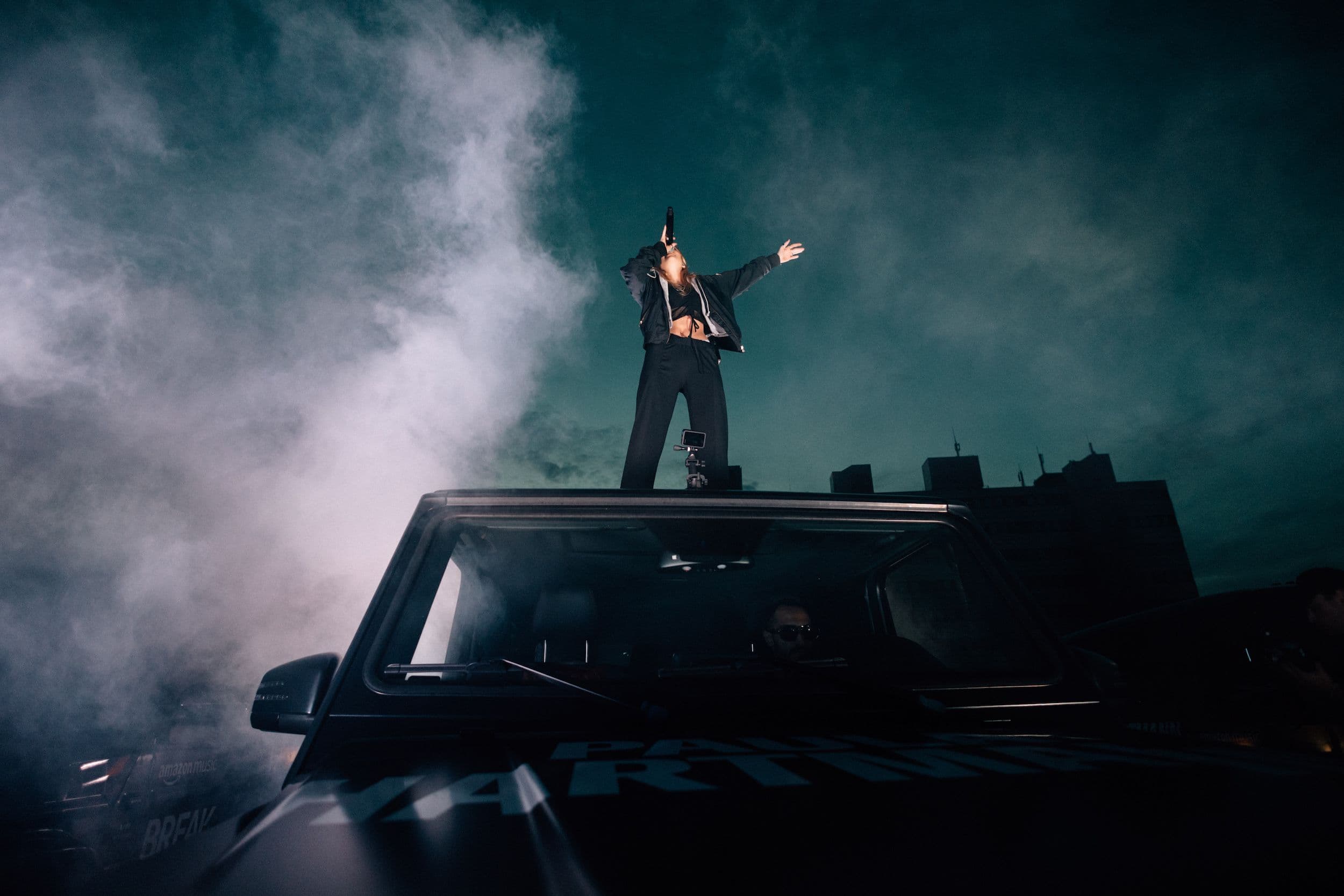 Foto von Paula Hartmann, die auf einem Auto bei Nebel ins Mikrofon singt