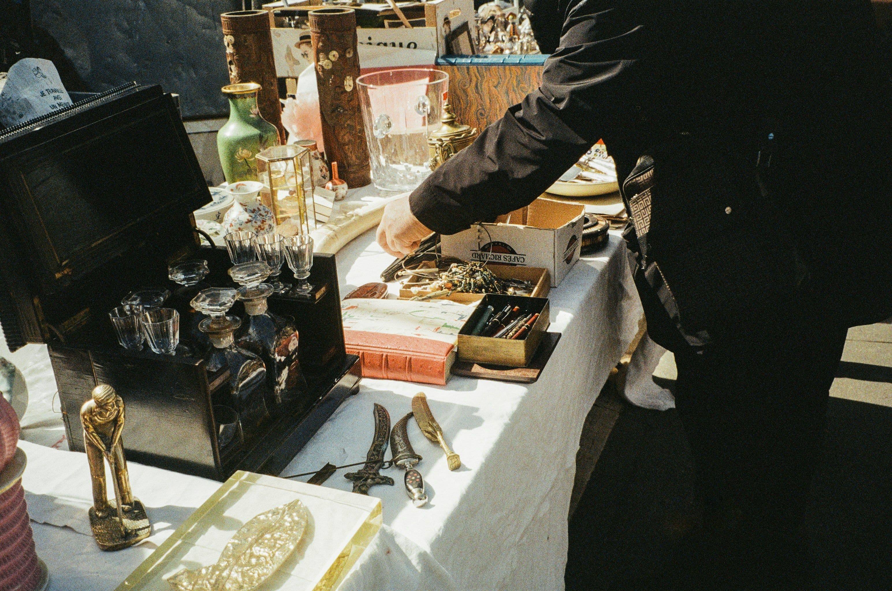 Eine Person steht an einem Flohmarkttisch, auf dem Antiquitäten liegen.