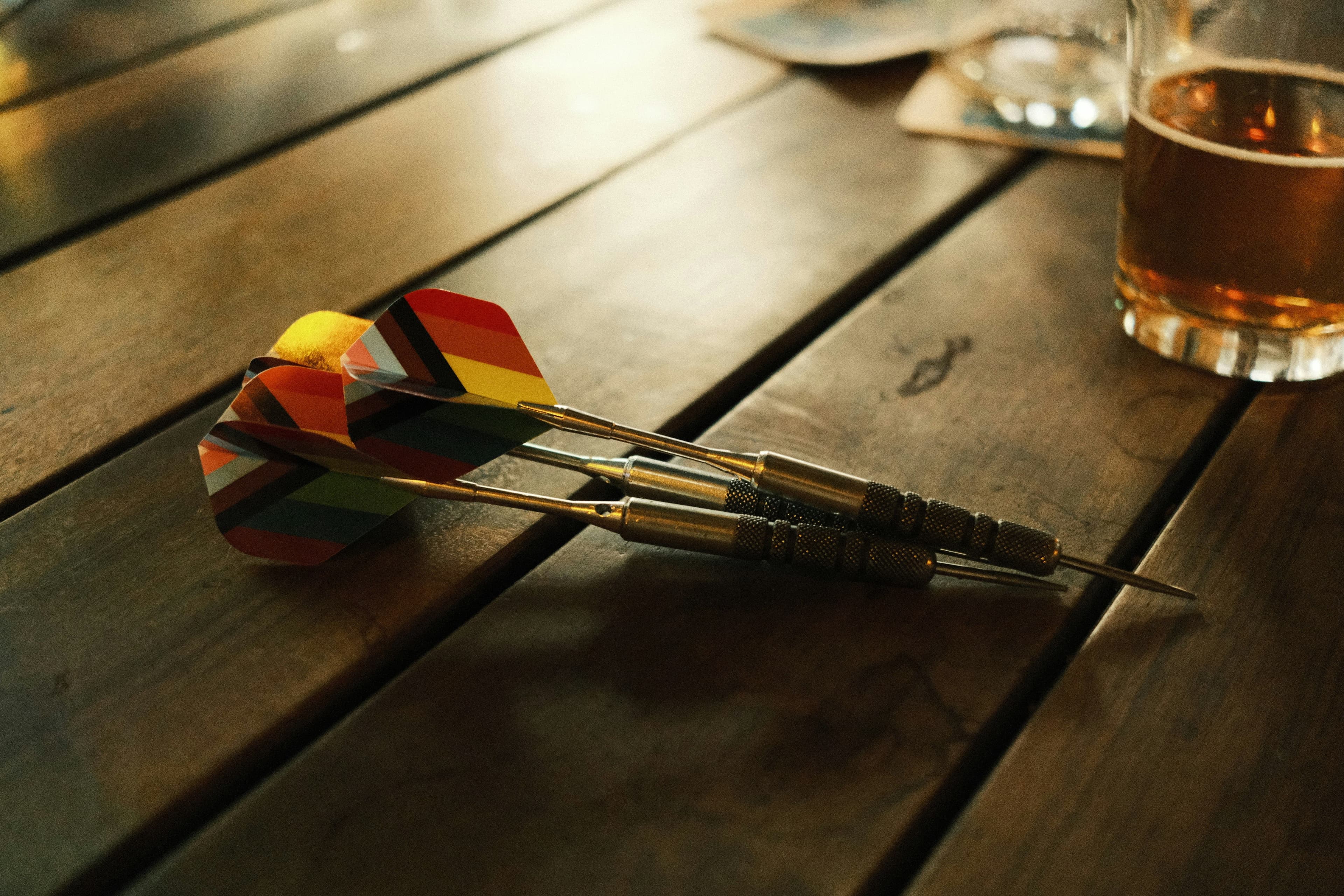 Darts-Pfeile und ein Glas Bier auf einem Holztisch