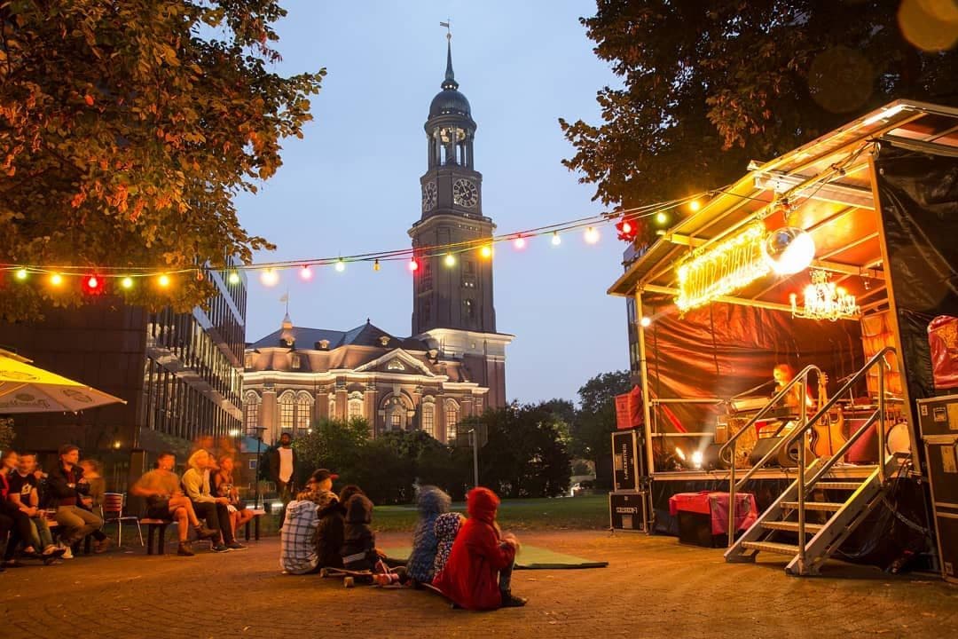 Menschen sitzen vor einer Open Air Bühne mit der Kirche St. Michaelis im Hintergrund