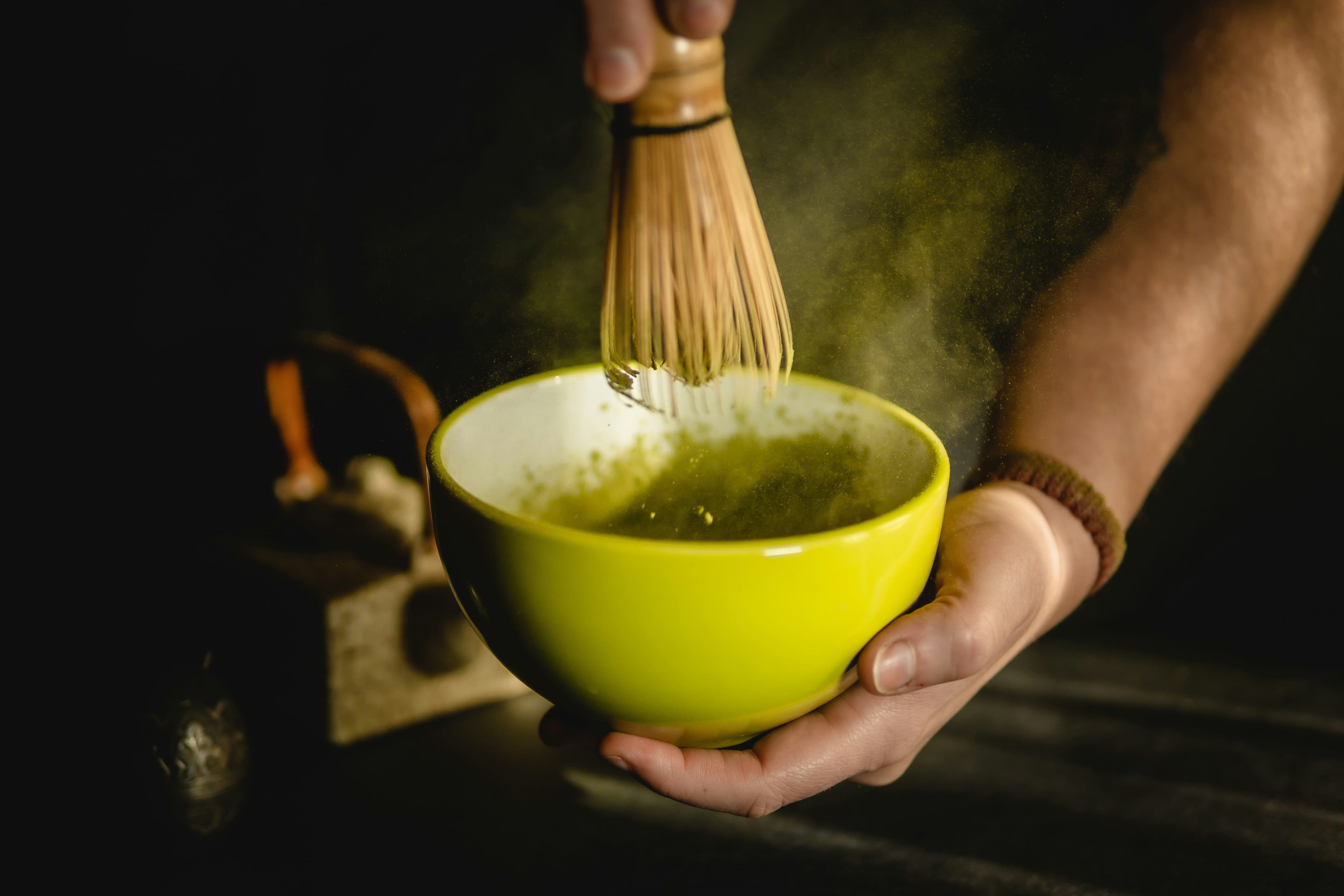 Eine Person schlägt Matcha-Pulver mit einem Matcha-Besen in einer Schale auf