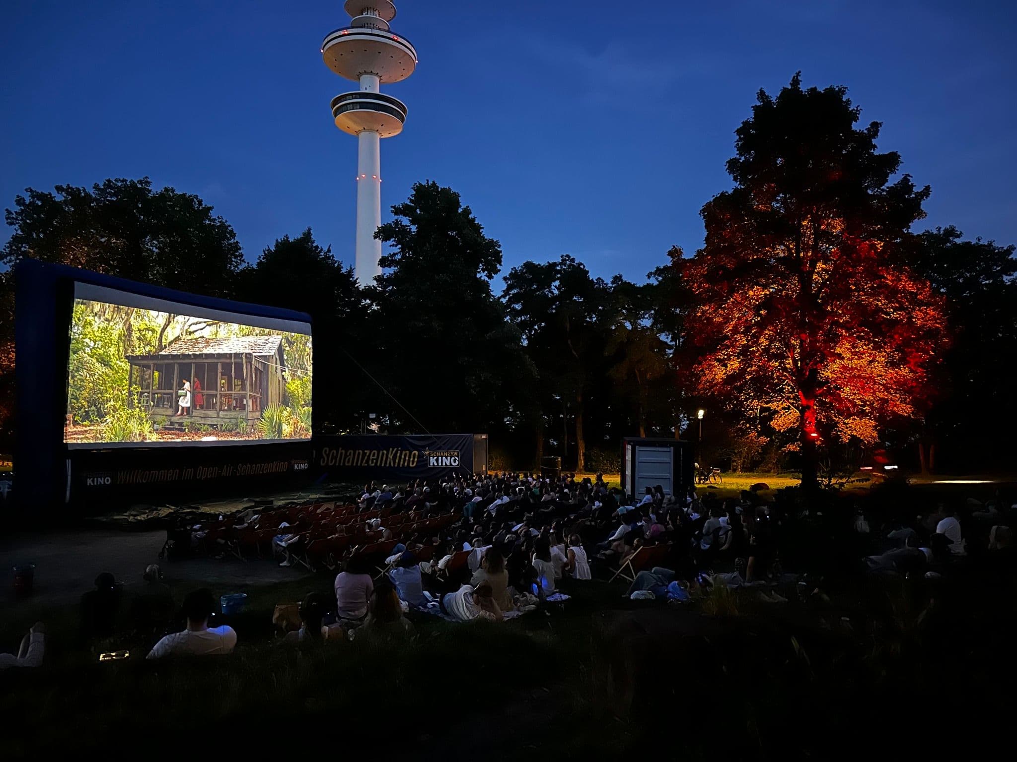 Menschen sitzen in einem Park vor einer großen Leinwand und schauen einen Film